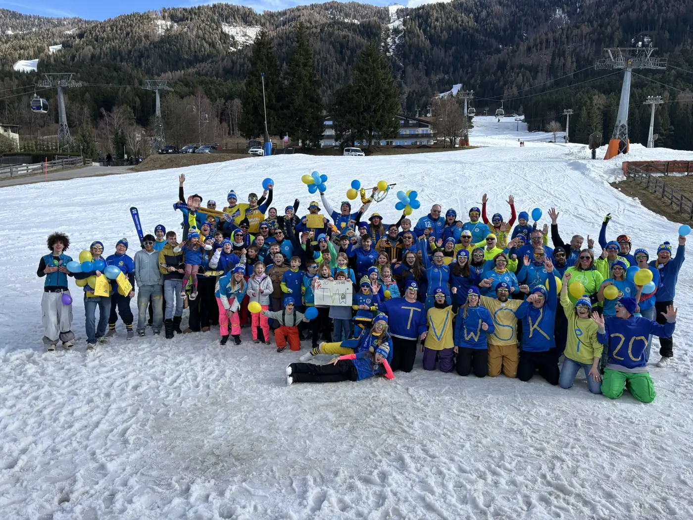 Grosse Gruppe des Turnvereins im Schnee, viele in blau-gelber Vereinskleidung mit Luftballons