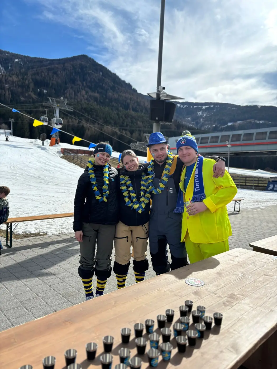 Vier Personen mit Blumenketten an einer Biertischgarnitur im Schnee